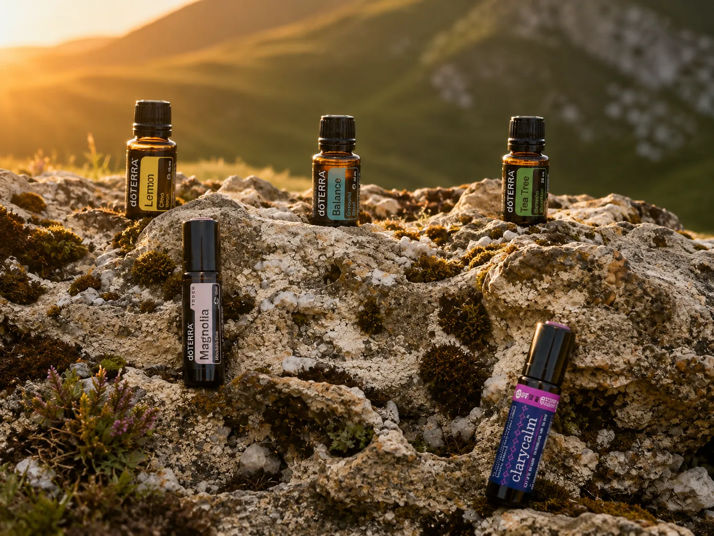 Fünf dōTERRA Fläschchen – Lemon, Balance, Tea Tree, Magnolia und ClaryCalm – auf einem bemoosten Felsrücken im Abendlicht.