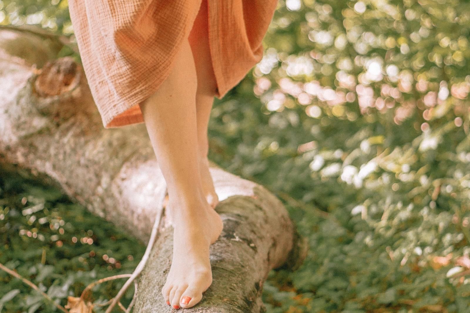 Barfüßige Person balanciert auf einem Baumstamm in der Natur.