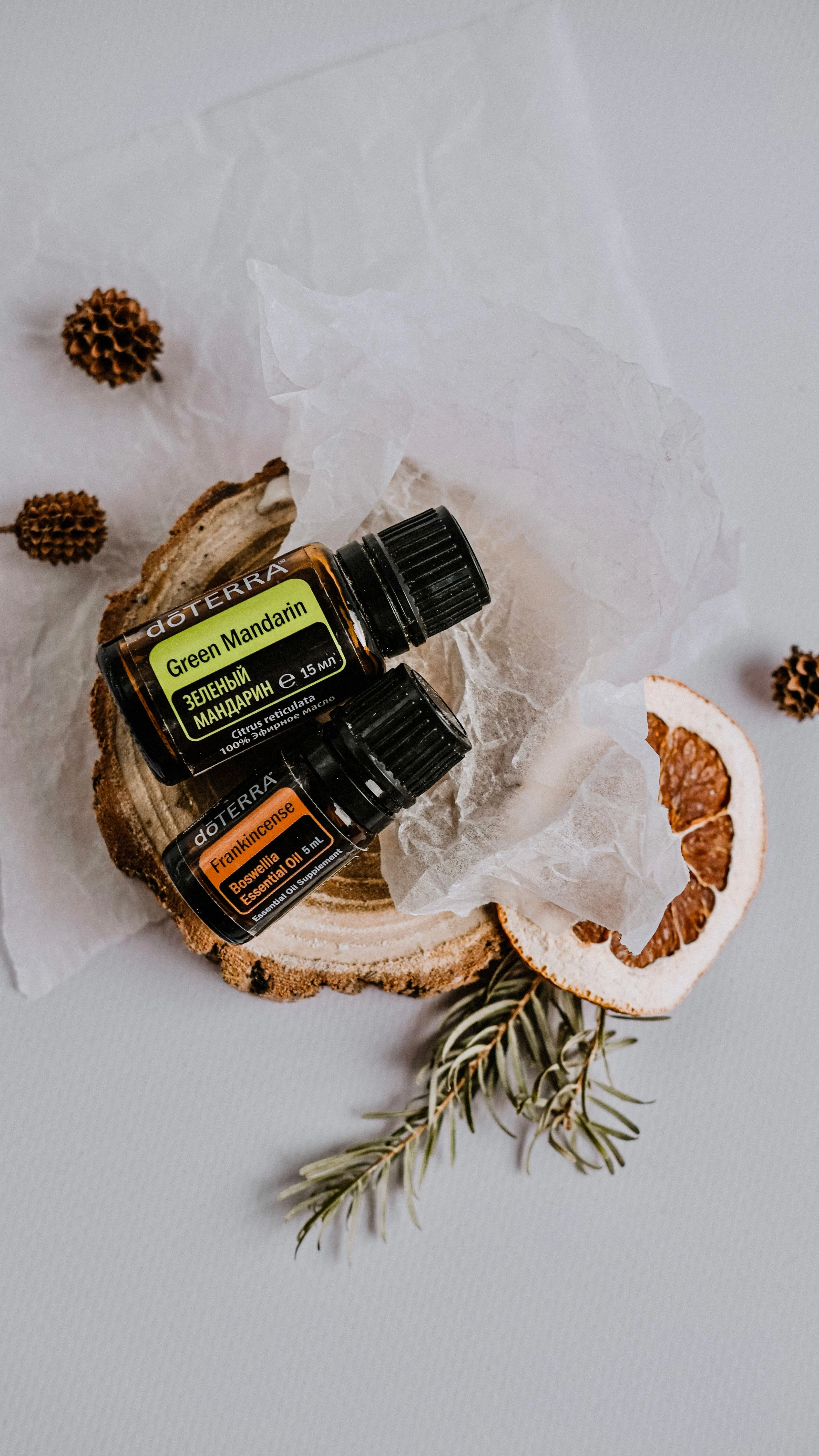 Zwei dōTERRA Fläschchen liegen auf einer Holzscheibe, daneben Seidenpapier, eine getrocknete Orangenscheibe und ein Rosmarinzweig.